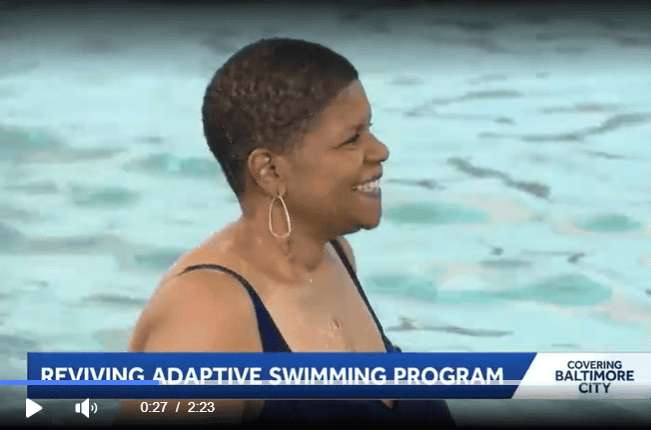 A woman in her bathing suit smiles at someone in the distance while in the pool.