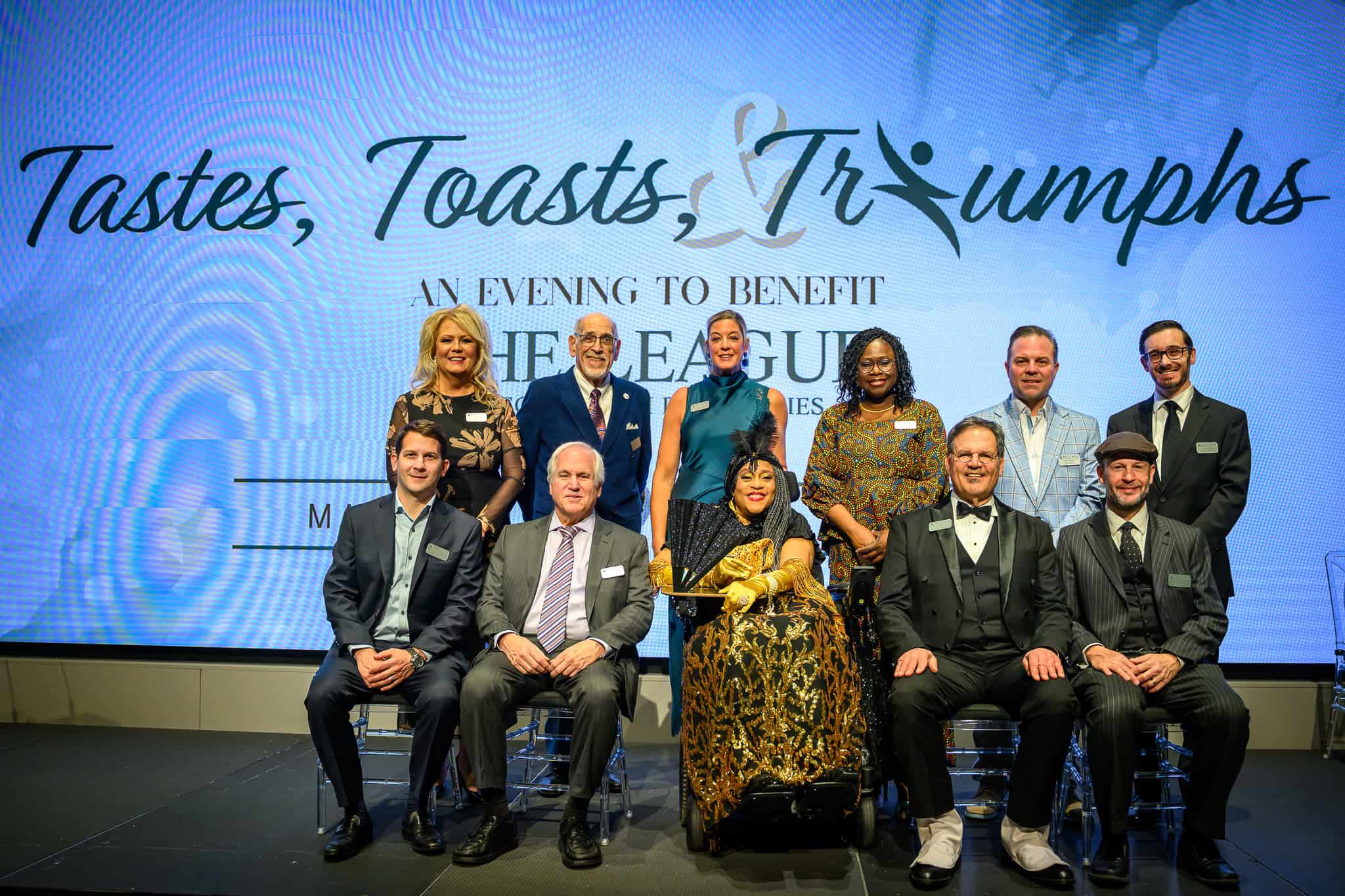 Men and women dressed in cocktail evening attire standing and seated on a stage.